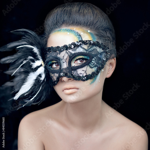 Mysterious beautiful girl in a black mask with feathers with green creative makeup in the studio on a dark background isolated