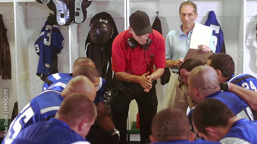 Football team gets a talk in the locker room from a coach 