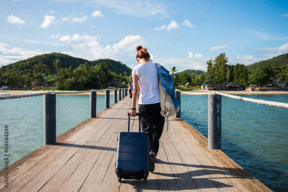 Fototapeta premium Girl tourist dragging luggage on a dock to tropical beach