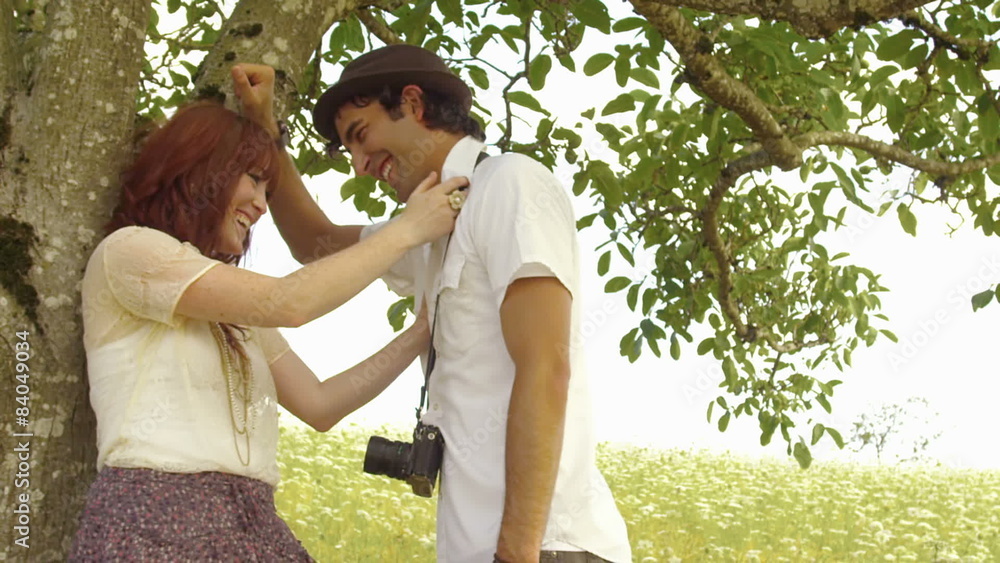 Young happy couple stand under a tree and smile at each other. Medium shot. Young happy couple stand under a tree and smile at each other. Medium shot.