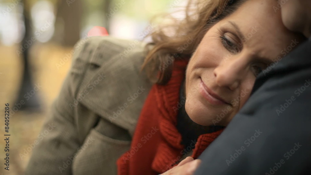 A couple sits on a park bench and the woman puts her head on his chest A couple sits on a park bench and the woman puts her head on his chest