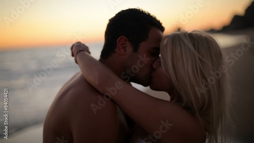 A cute couple kisses on the beach while the sun sets photo