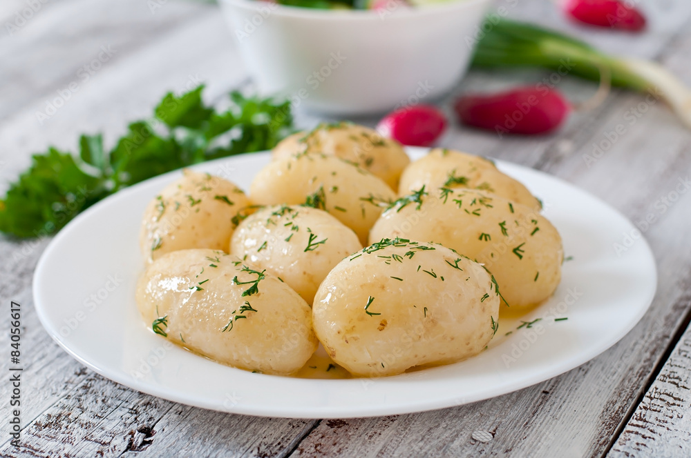 Fototapeta premium Young boiled potatoes with butter and dill on a white plate