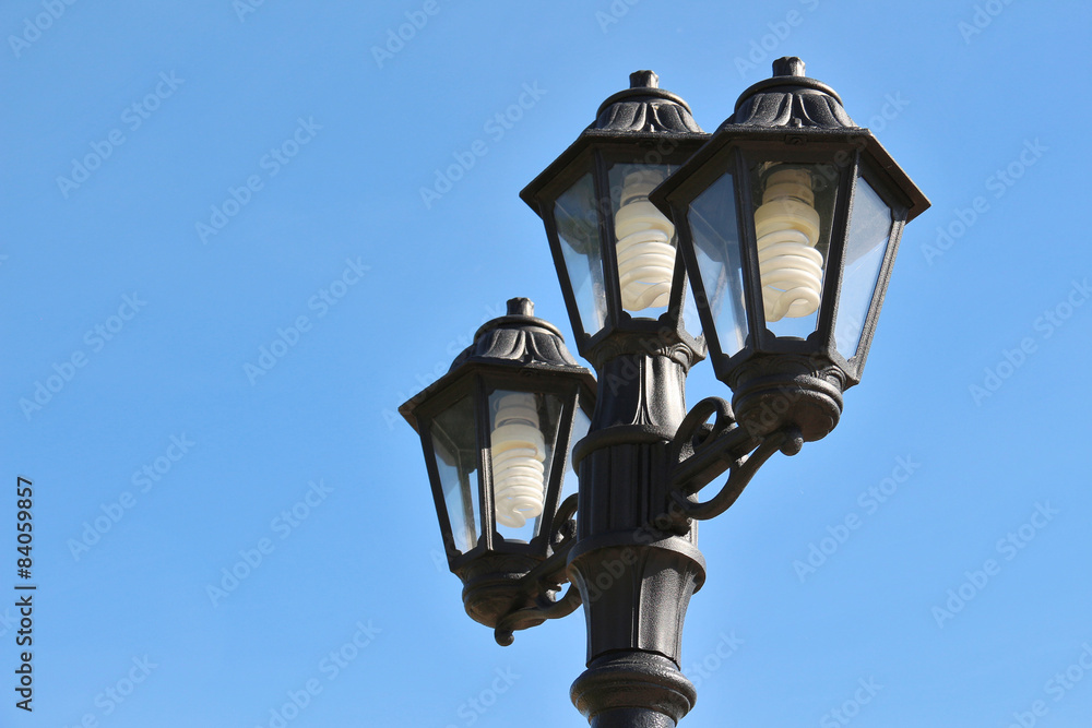 Three vintage street lamps against bright blue sky