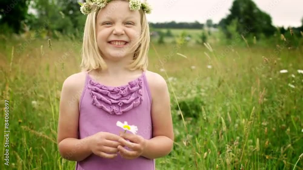 A blonde girl stands in a field during the day with followers in her hair