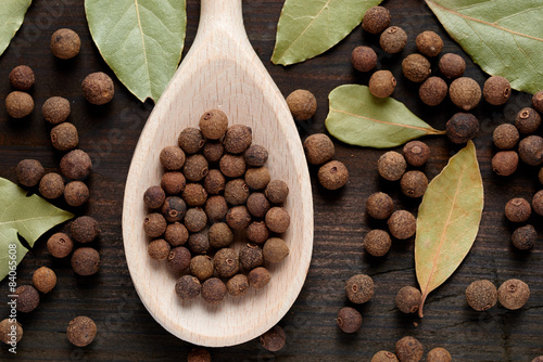 Photos allspice on a wooden spoon surrounded by a bay leaf and allspice