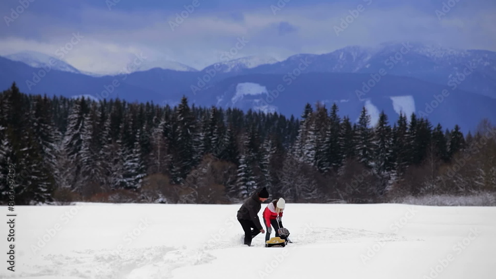 A mother and father walk through a snow covered field with their son and a sled A mother and father walk through a snow covered field with their son and a sled