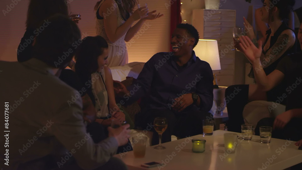 A group of friends sit together talking and laughing at a house party