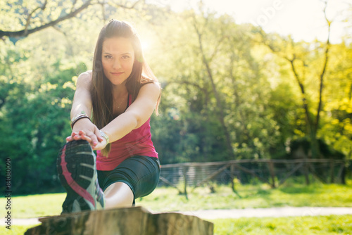 Young woman stretching outdoors in a park with flair sunny light