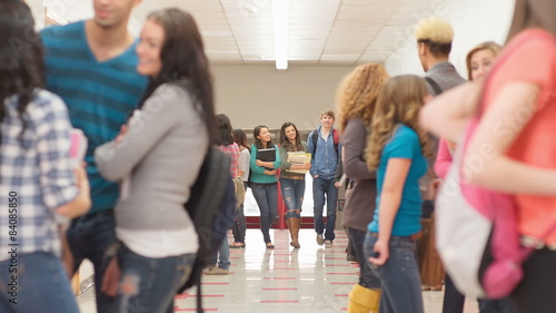 Friends walk through a crowd of students standing in the hallway before class photo