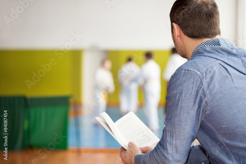 Father reading, witing for his kids training martial arts