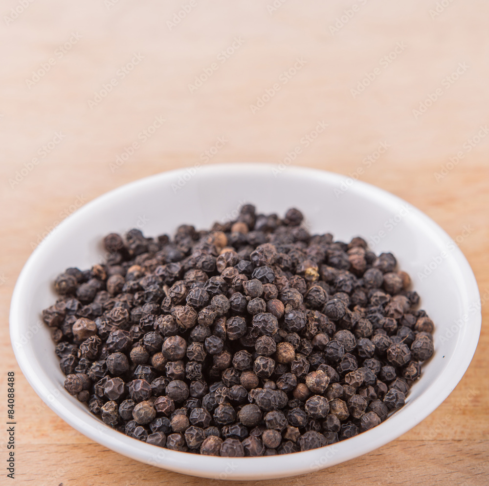 Black pepper in white bowl on wooden surface Black pepper in white bowl on wooden surface