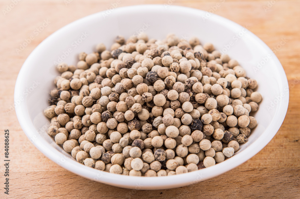 White pepper in white bowl on wooden surface White pepper in white bowl on wooden surface