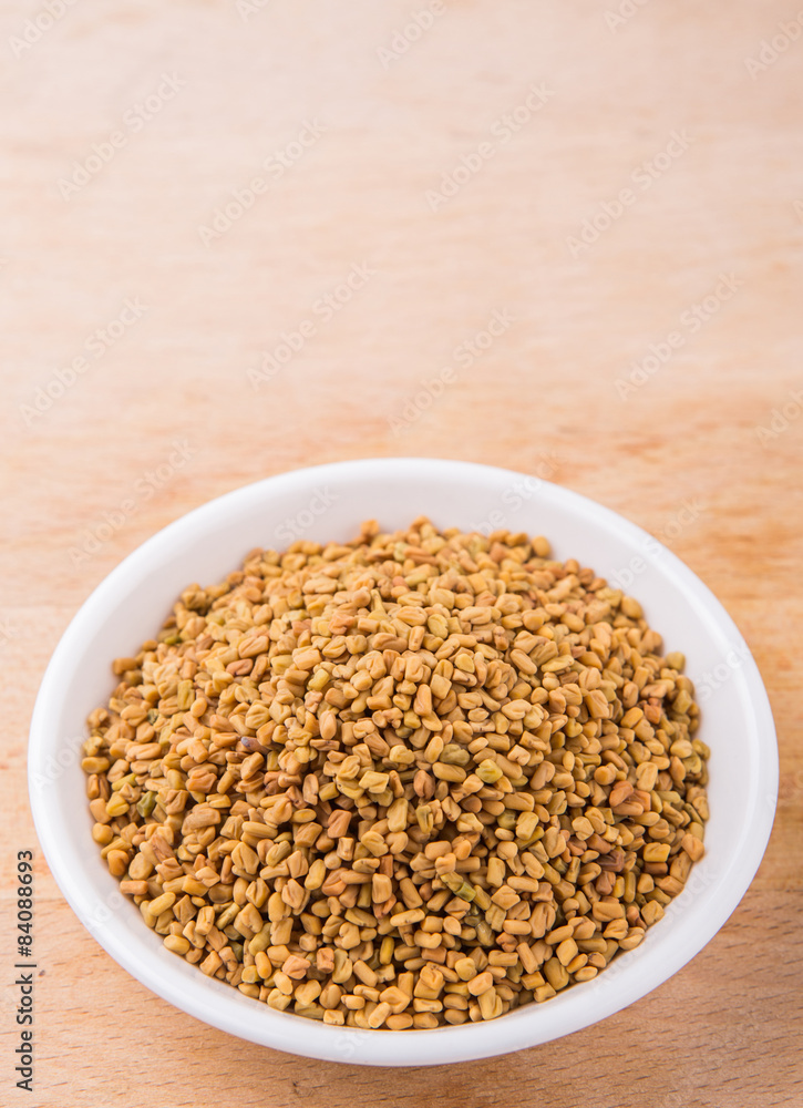 Fenugreek seeds in white bowl on wooden surface Fenugreek seeds in white bowl on wooden surface