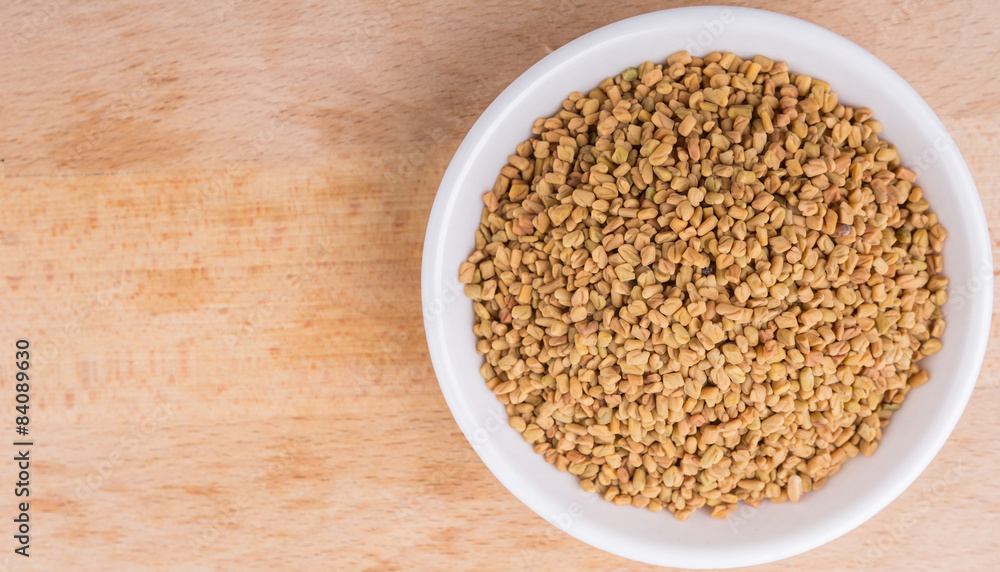 Fenugreek seeds in white bowl on wooden surface Fenugreek seeds in white bowl on wooden surface