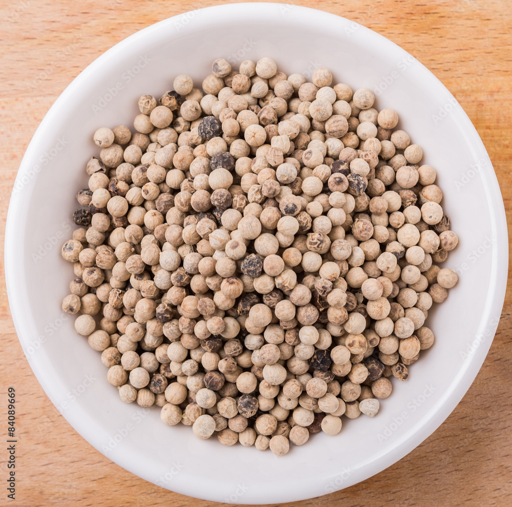White pepper in white bowl on wooden surface White pepper in white bowl on wooden surface