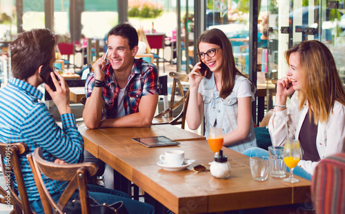 Group of young people sitting at a cafe, talking over phones