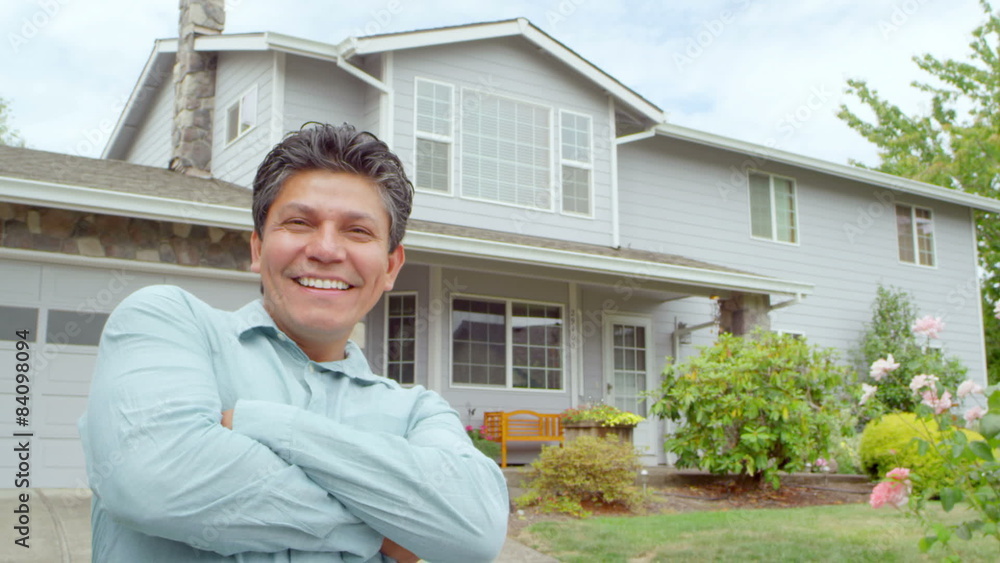 An excited hispanic man smiles at the camera and then walks up his driveway to go into his house