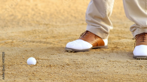 A golfer takes a swing at a golf ball while in a sand trap