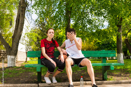 Young Couple Sitting on Park Bench with Basketball