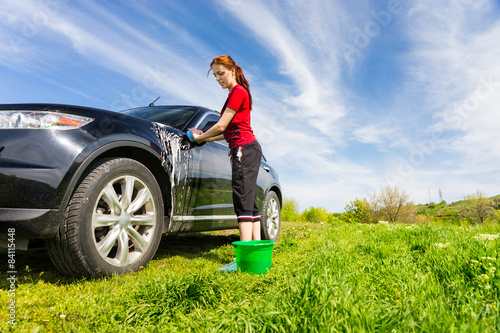 Woman Washing Black Car in Field with Soapy Sponge