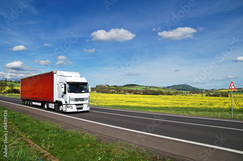 Truck on the road between yellow flowering rapeseed field