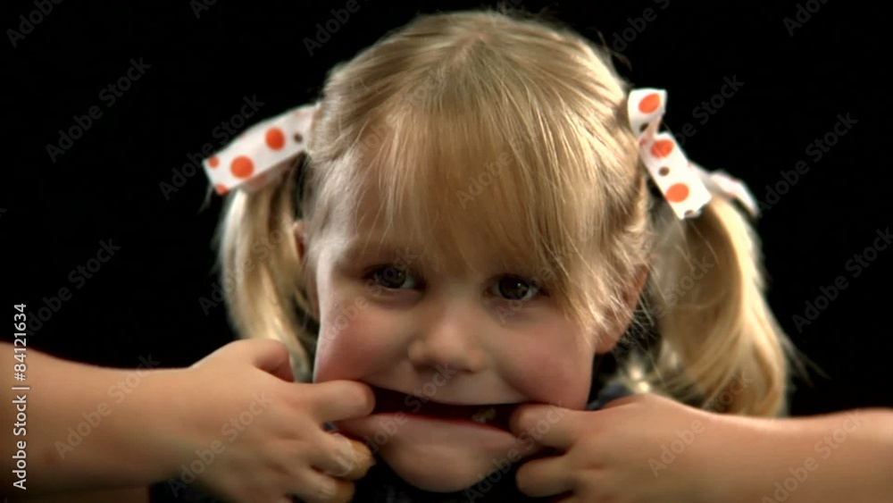 A young blonde girl with pigtails pulls her mouth to make a funny face A young blonde girl with pigtails pulls her mouth to make a funny face