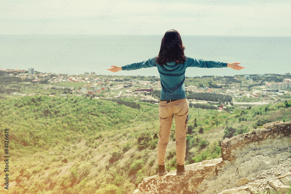 Traveler woman standing with raised arms on peak of rock