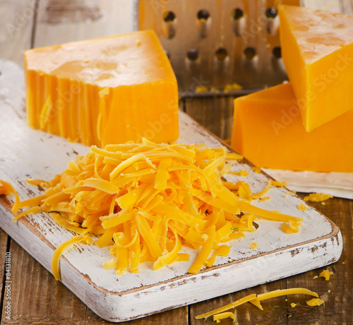 Grated Cheddar Cheese on wooden Cutting Board.