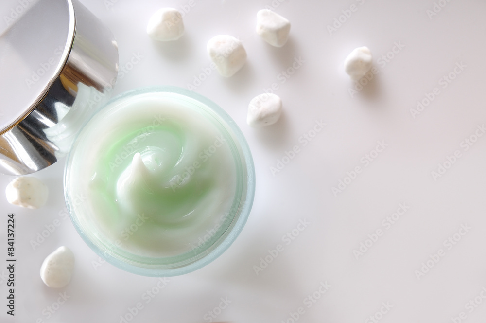 Fototapeta premium Cream jar open and small white stones isolated top view