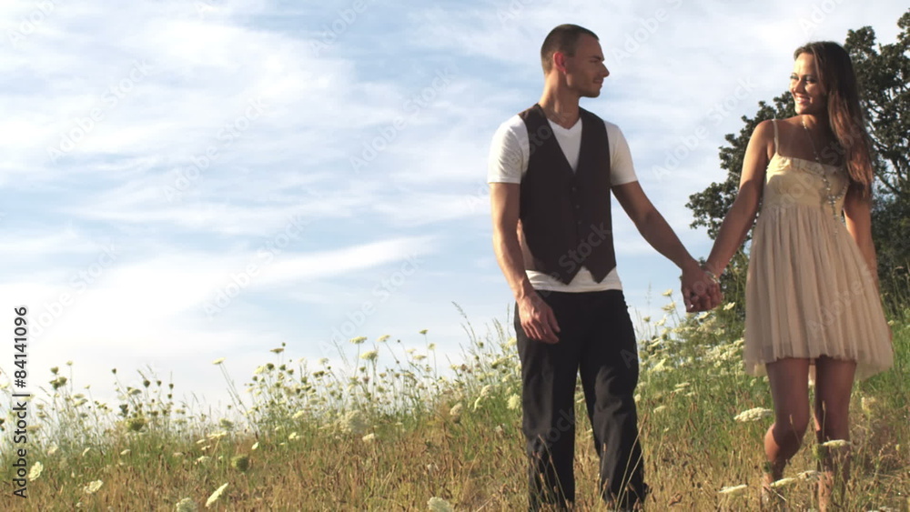Happy couple playfully walk through field of flowers. Wide shot. Happy couple playfully walk through field of flowers. Wide shot.