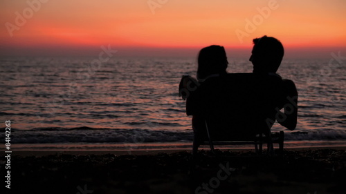 A couple on the beach in a lawn chair embrace each other watching the sunset