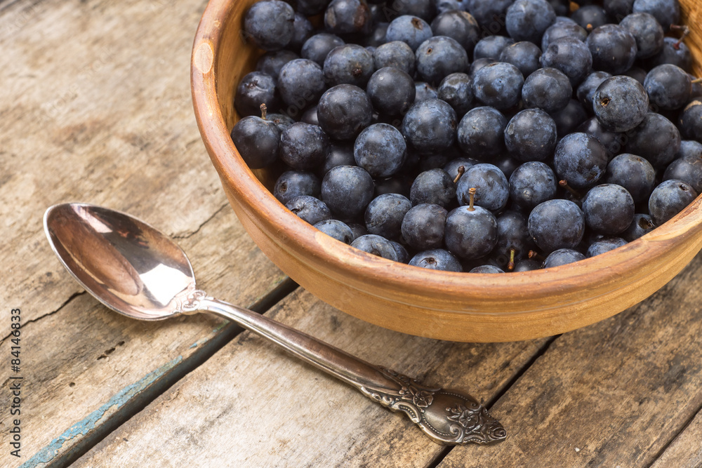 Fresh blackthorn in clay bowl with silverspoon on wooden table Fresh blackthorn in clay bowl with silverspoon on wooden table