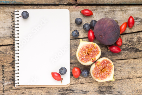 Fresh wild berries and figs with blank notebook on wood 