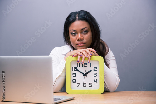 Tired businesswoman sitting at the table with clock