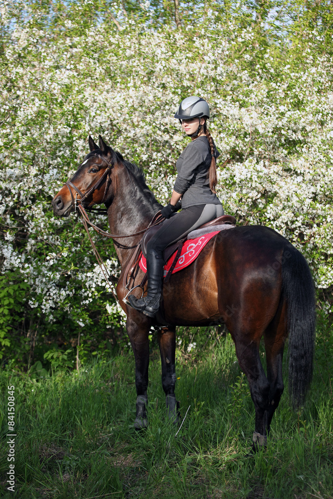 Girl with bay riding horse in a lush garden

