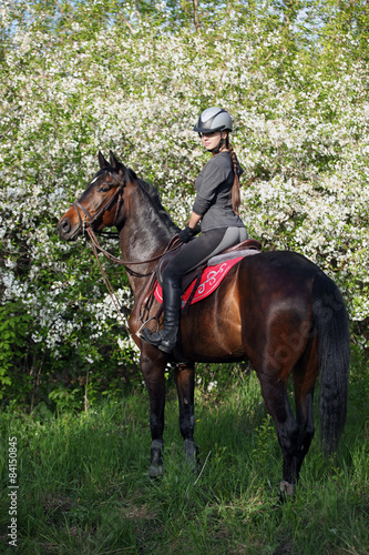 Girl with bay riding horse in a lush garden 