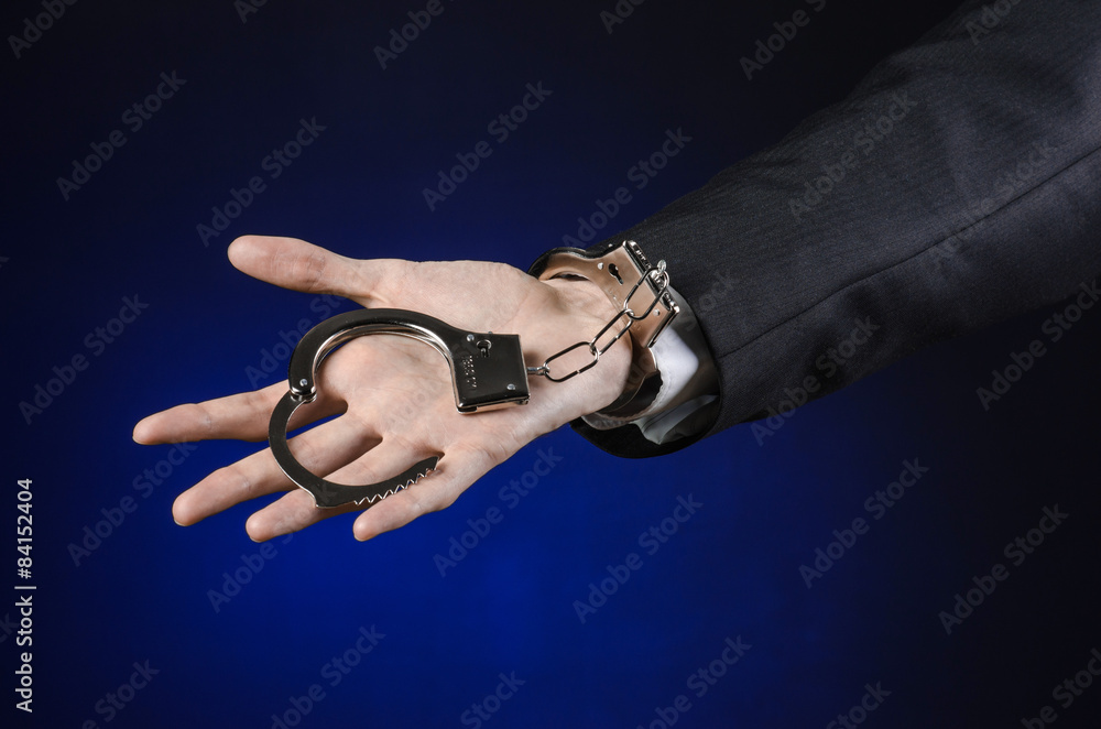Fototapeta premium businessman in a black suit with handcuffs on his hands studio
