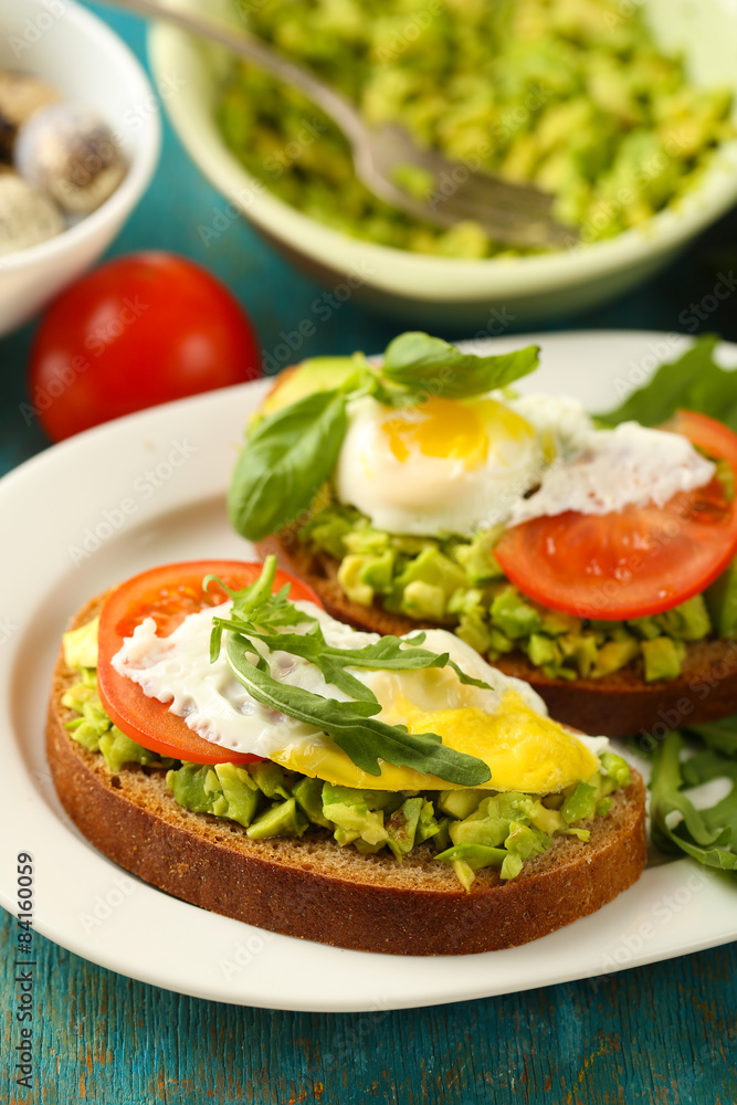 Tasty sandwiches with egg, avocado and vegetables on plate, on wooden background