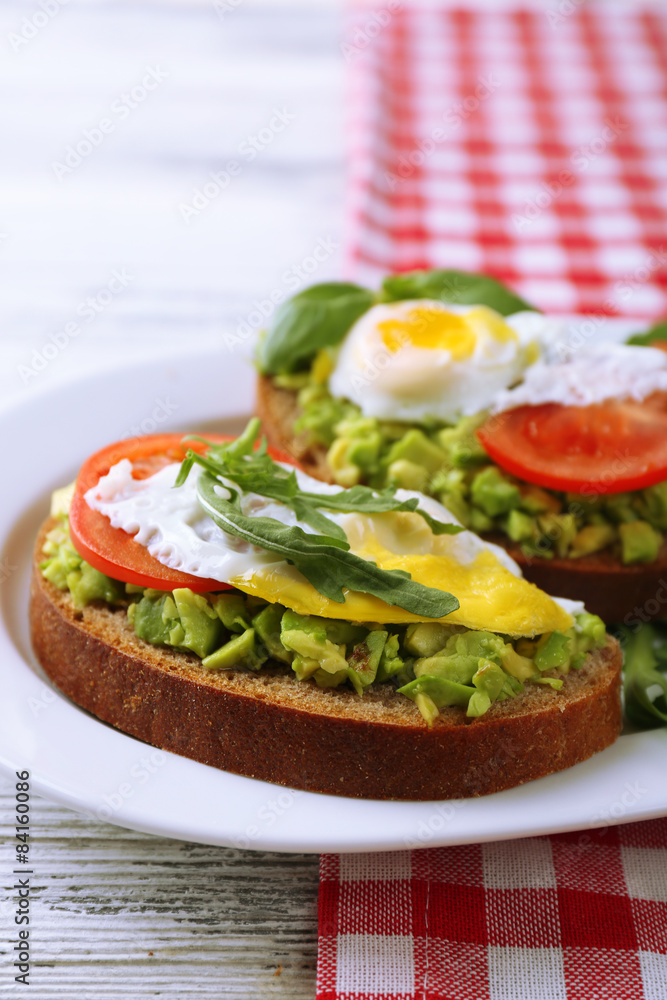 Tasty sandwiches with egg, avocado and vegetables on plate, on wooden background