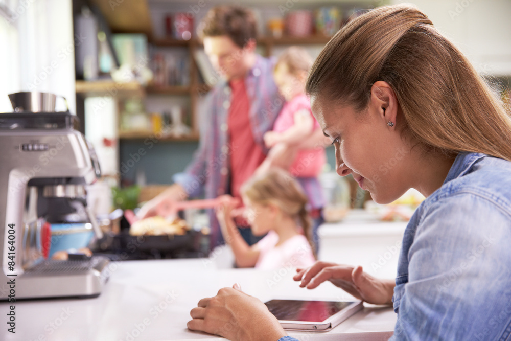 Father Cooks Family Meal Whilst Mother Uses Digital Tablet Father Cooks Family Meal Whilst Mother Uses Digital Tablet