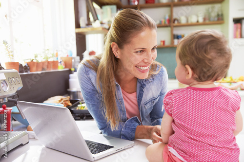 Mother With Young Daughter Using Laptop In Kitchen