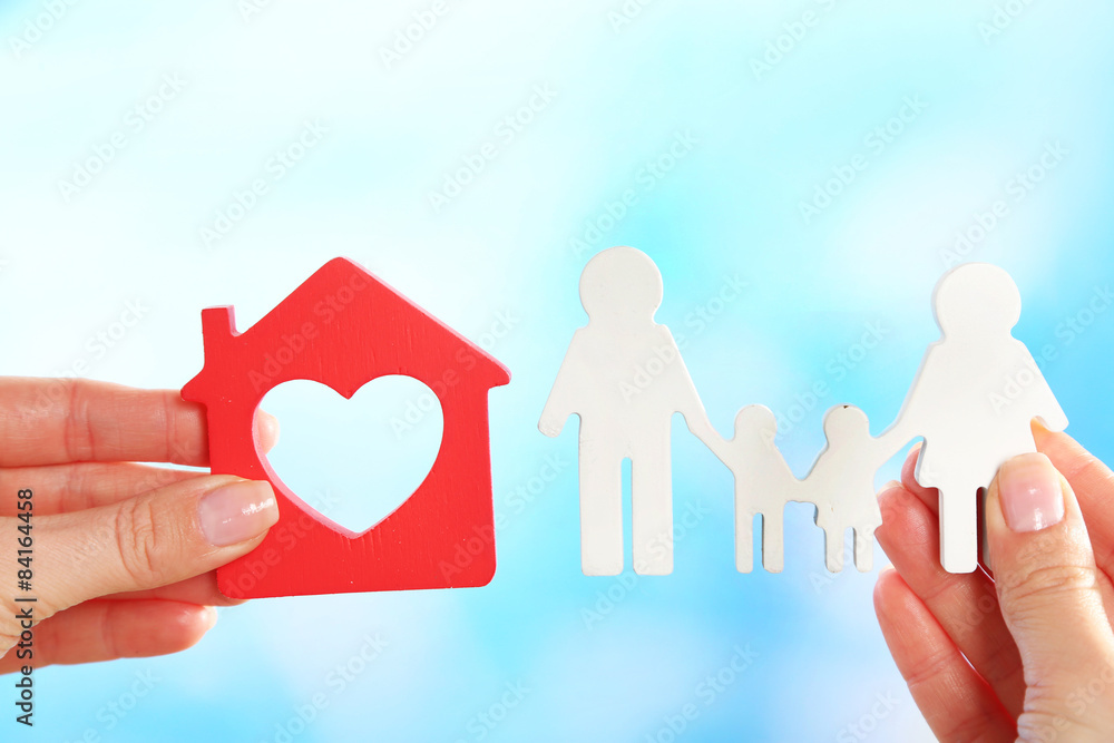 Female hands holding model of house and paper family on bright background Female hands holding model of house and paper family on bright background