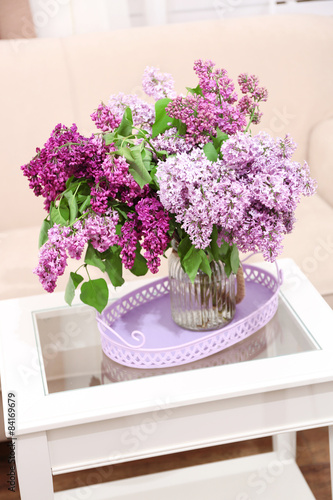 Beautiful lilac flowers in vase on table of interior background