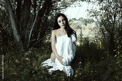 Pale woman in white dress on the ground, dark mystery scene