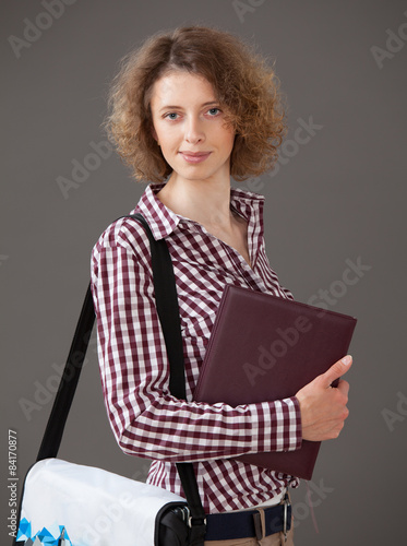Portrait of a young woman holding a book and a briefcase