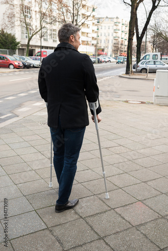 Man Walking On Street Using Crutches