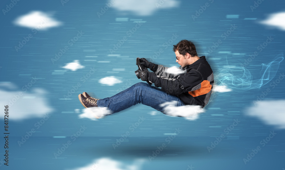 Funny racedriver young man driving between clouds concept Funny racedriver young man driving between clouds concept