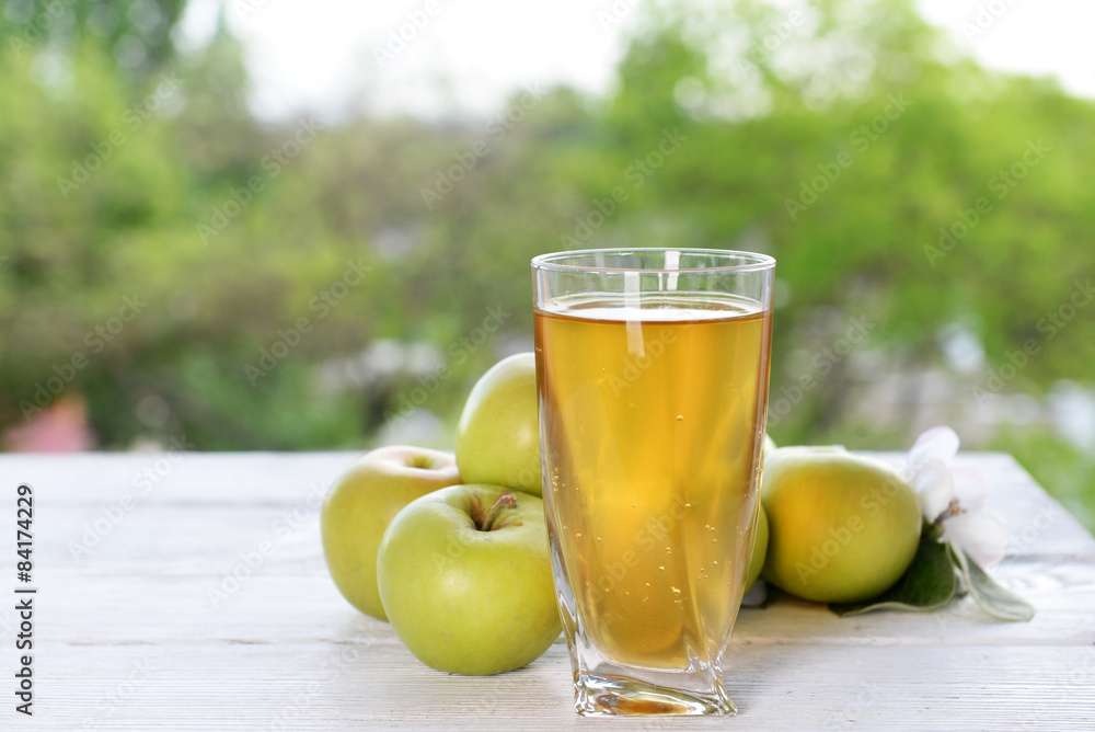 Glass of apple juice and apples on wooden table, on nature background Glass of apple juice and apples on wooden table, on nature background