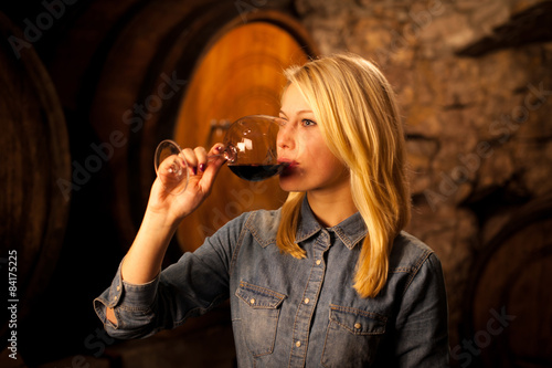 Картината върху платно Beautiful young blond woman tasting red wine in a wine cellar